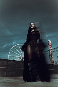 a woman in a black dress standing in front of a ferris wheel