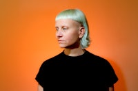 a woman with blond hair standing in front of an orange wall